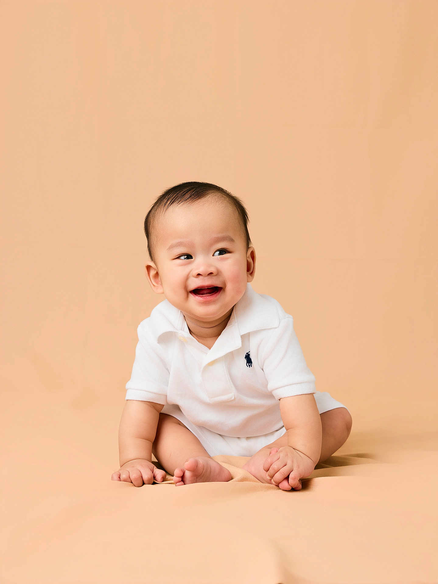 Rei is registered to the contest to win money with this photo: baby, child, smiling, happy, sitting, white_clothing, polo_shirt, infant, cute, portrait, studio, beige_background, skin, face, hands, feet, young, expression, one_person, indoors