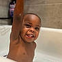 toddler, bathtub, bath, child, smiling, happy, water, soap, arm, raised_hand, teeth, skin, face, indoor, tile, bathroom, toy, blurred_background, cute, playful