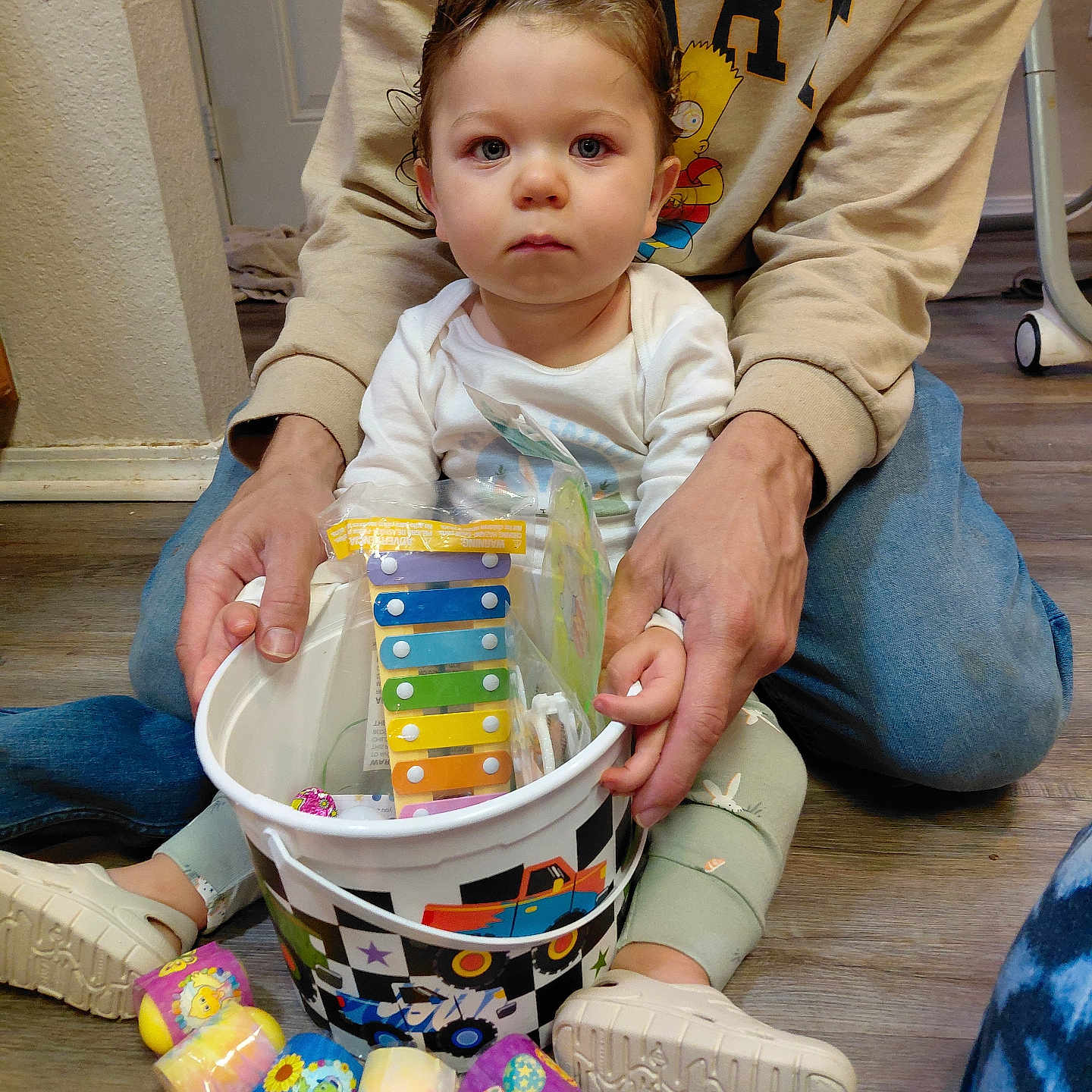 Nathaniel joined the competition — help win amazing prizes! toddler, child, adult, toy_bucket, toys, indoor, floor, casual_clothing, sitting, pastel_colors, colorful, hand_holding, wood_floor, shoes, person, young_child, expressionless, supporting_hands, basket, plastic_toys