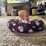 baby, infant, cushion, floral_pattern, carpet, living_room, television, cartoon, furniture, decor, blanket, toy, home, floor, person, cute, child, striped_clothing, relaxing, indoor