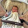 baby, stroller, blanket, outdoor, child, face, infant, clothing, canopy, fabric, seat, nature, wood, pine_needles, hands, relaxed, cute, comfort, portrait, leisure