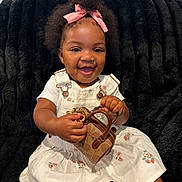 Kadale is registered to the contest to win money with this photo: baby, child, infant, portrait, smiling, happy, bow, pink_bow, curly_hair, black_blanket, dress, floral_dress, overalls, handbag, purse, fashion, sitting, indoors, closeup, photography