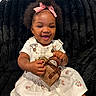 baby, child, infant, portrait, smiling, happy, bow, pink_bow, curly_hair, black_blanket, dress, floral_dress, overalls, handbag, purse, fashion, sitting, indoors, closeup, photography