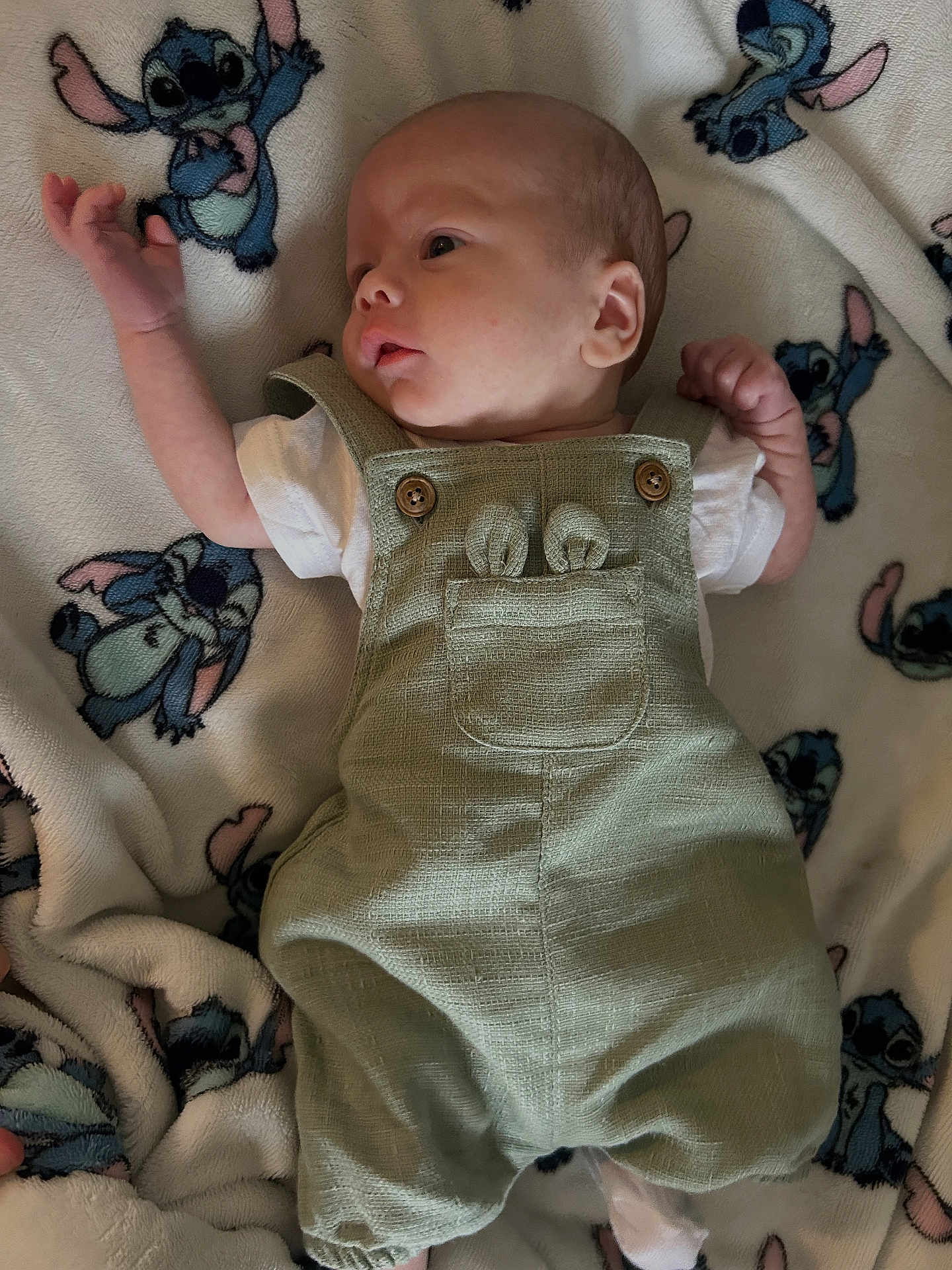 Cameron is registered to the contest to win money with this photo: baby, infant, overalls, green_clothing, blanket, stitch_character, cartoon_pattern, lying_down, cute, small_hands, soft_texture, fabric, head, face, newborn, child, sleepwear, comfort, resting, toddler
