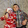 baby, child, sibling, plaid_shirt, festive_pajamas, reindeer_pattern, hat, blanket, bedroom, indoor, cuddling, family, portrait, laying_down, casual_clothing, happy, cute, smile, cozy, home