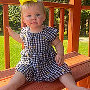 Paisley is registered to the contest to win money with this photo: toddler, child, yellow_bow, outdoor, bench, wooden_bench, dress, checkered_dress, greenery, sunlight, summer, portrait, baby, cute, sitting, smiling, nature, daylight, park, happy