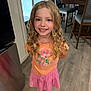 child, girl, smiling, blonde_hair, curly_hair, tshirt, skirt, barefoot, indoor, kitchen, floor, wooden_floor, furniture, chair, table, happy, portrait, standing, person, casual_clothing