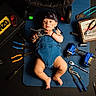 automotive, baby, bandana, blue_mat, child, drill, garage, humorous, indoor, infant, lying_down, mechanic, overalls, pliers, portrait, screwdriver, toolbox, tools, workshop, wrench