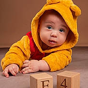 Enzo joined the competition — help win amazing prizes! baby, child, hooded_outfit, yellow_clothing, blue_eyes, wooden_blocks, floor, cute, portrait, indoor, soft_texture, plush, face, hands, curious, infant, toddler, studio_lighting, warm_colors, expression