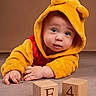 baby, child, hooded_outfit, yellow_clothing, blue_eyes, wooden_blocks, floor, cute, portrait, indoor, soft_texture, plush, face, hands, curious, infant, toddler, studio_lighting, warm_colors, expression