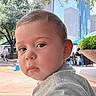 Enzo is registered to the contest to win money with this photo: baby, child, city, daylight, eyes, face, gray_shirt, infant, looking_at_camera, outdoor, park, photography, planter, portrait, sidewalk, skyscrapers, sunlight, toddler, trees, urban