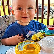 Nicholas is registered to the contest to win money with this photo: baby, child, smiling, blue_eyes, toy, activity_walker, outdoor, porch, railing, car, clothing, blue_shirt, happy, infant, person, cute, play, seat, daylight, face
