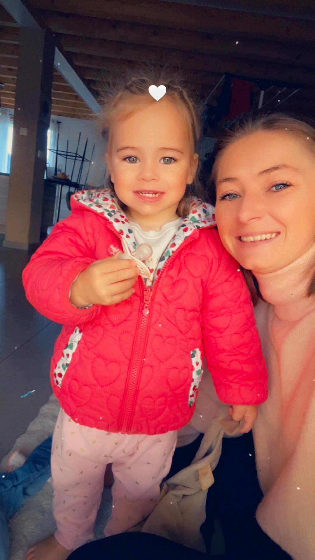 Kira a rejoint le concours — aidez-le/la à gagner de superbes lots ! child, toddler, woman, smiling, indoor, red_jacket, pacifier, pink_pants, heart_pattern, person, face, portrait, floor, wooden_ceiling, natural_light, cozy, happy, casual_clothing, family, home