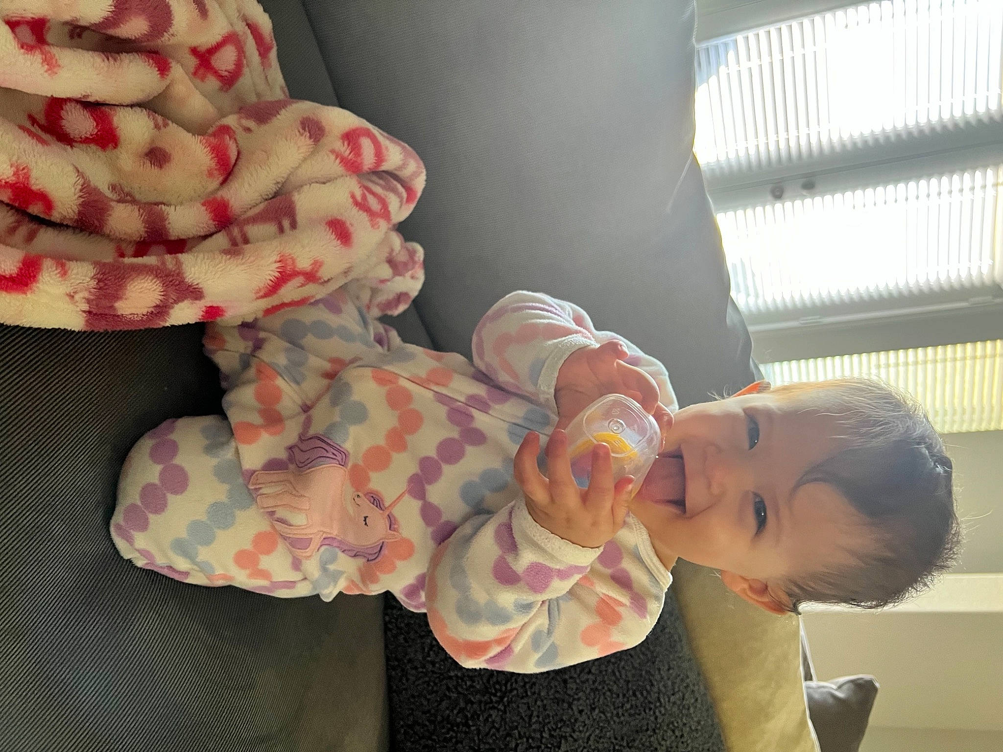 Emery is registered to the contest to win money with this photo: baby, baby_products, baby_toddler_clothing, carmine, child, comfort, finger, happy, linens, nail, pattern, peach, person, room, smile, sock, stuffed_toy, thumb, toddler, window_blind