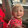 toddler, child, smiling, red_shirt, car_interior, seatbelt, window, portrait, happy, face, short_hair, daylight, casual_clothing, seated, person, indoors, photography, cute, expression, young_child
