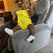 Kaycee joined the competition — help win amazing prizes! toddler, child, yellow_outfit, sock, couch, living_room, carpet, adult_hand, curtain, furniture, person, home_interior, playful, smiling, indoors, support, window, seat, baby, expression