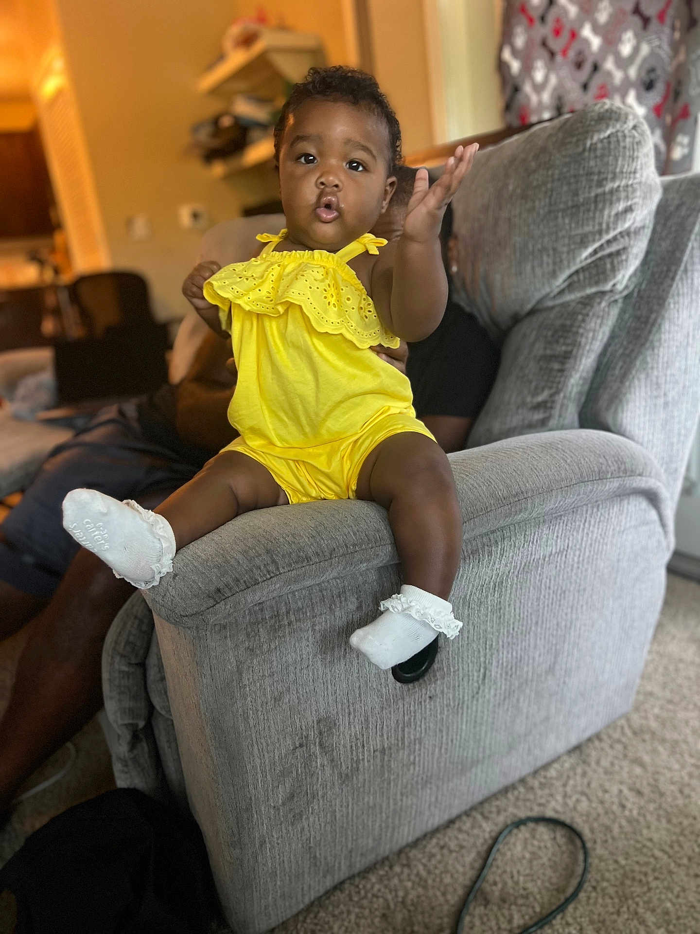 Kaycee joined the competition — help win amazing prizes! toddler, child, yellow_outfit, sock, couch, living_room, carpet, adult_hand, curtain, furniture, person, home_interior, playful, smiling, indoors, support, window, seat, baby, expression