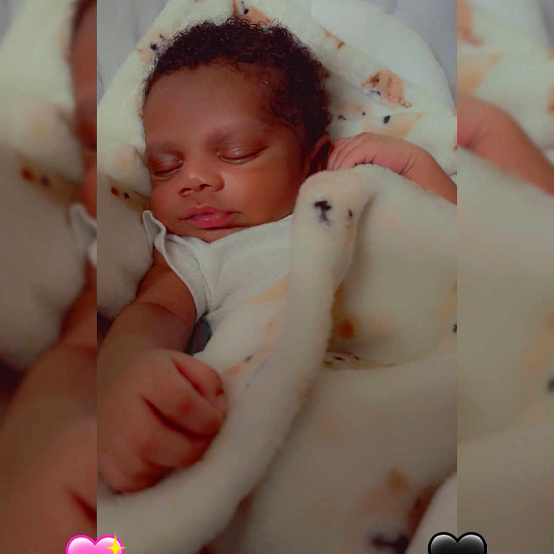 Brian is registered to the contest to win money with this photo: baby, sleeping, blanket, infant, curly_hair, peaceful, cozy, closeup, soft_texture, indoors, heart_emoji, blue_hearts, pink_hearts, black_hearts, wrapped, cute, resting, child, portrait, adorable