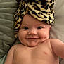 baby, smile, cheeks, towel, leopard_print, headwear, bed, pillow, skin, infant, cute, portrait, lying_down, happy, indoors, child, face, closeup, naked_torso, expression