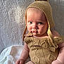 Koa is registered to the contest to win money with this photo: baby, child, knitwear, hat, pom_pom, beige, texture, blanket, portrait, indoor, cute, infant, soft_light, expression, hands, skin, sitting, warm_clothing, closeup, person
