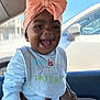 Azira joined the competition — help win amazing prizes! baby, infant, smile, pink_bow, headwrap, bib, white_shirt, parent_hand, car_interior, window, seat, portrait, happy, cute, tongue, cheek, dark_skin, daylight, earring, baby_clothing