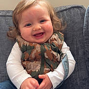 Kyson joined the competition — help win amazing prizes! toddler, child, smiling, happy, curly_hair, camouflage_vest, white_shirt, blue_jeans, sitting, couch, indoor, rosy_cheeks, face, person, clothing, casual, cute, young_child, portrait, cozy