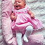 baby, infant, smiling, pink_dress, white_tights, headband, flower_headband, blanket, soft_texture, lying_down, happy, cute, child, portrait, indoors, fluffy_surface, rolled_blanket, small_hands, small_feet, cheerful