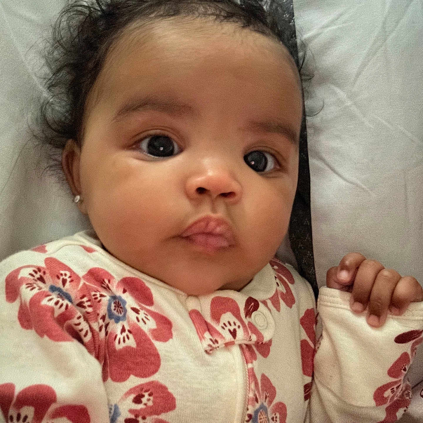 Dazaiah is registered to the contest to win money with this photo: baby, child, cozy, curly_hair, cute, expression, eyes, face, floral_pattern, hand, indoors, infant, lying_down, newborn, onesie, person, portrait, skin, sleepwear, soft