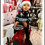 toddler, child, toy_car, christmas_hat, christmas_sweater, holiday_decorations, plush_bear, wrapped_gifts, white_rug, festive, indoor, smiling, seasonal, cute, red, black_pants, blue_eyes, decor, portrait, winter