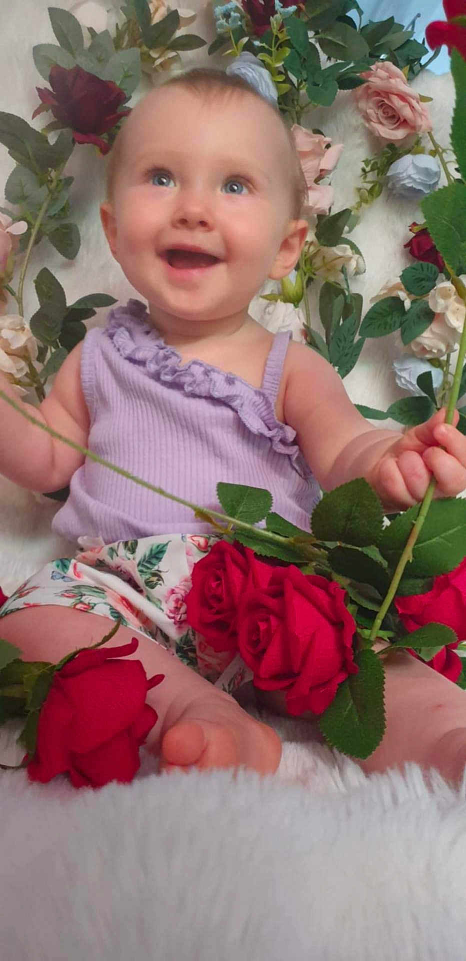 Ilona a rejoint le concours — aidez-le/la à gagner de superbes lots ! baby, child, smiling, flowers, roses, purple_top, floral_shorts, green_leaves, happy, sitting, cute, portrait, nature, plant, petals, skin, foot, hand, indoors, colorful