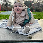 Oaklyn-Jay joined the competition — help win amazing prizes! baby, child, smiling, hat, beanie, jacket, clothing, blanket, outdoor, playground, swing, grass, trees, happy, cute, winter, person, footwear, face, nature
