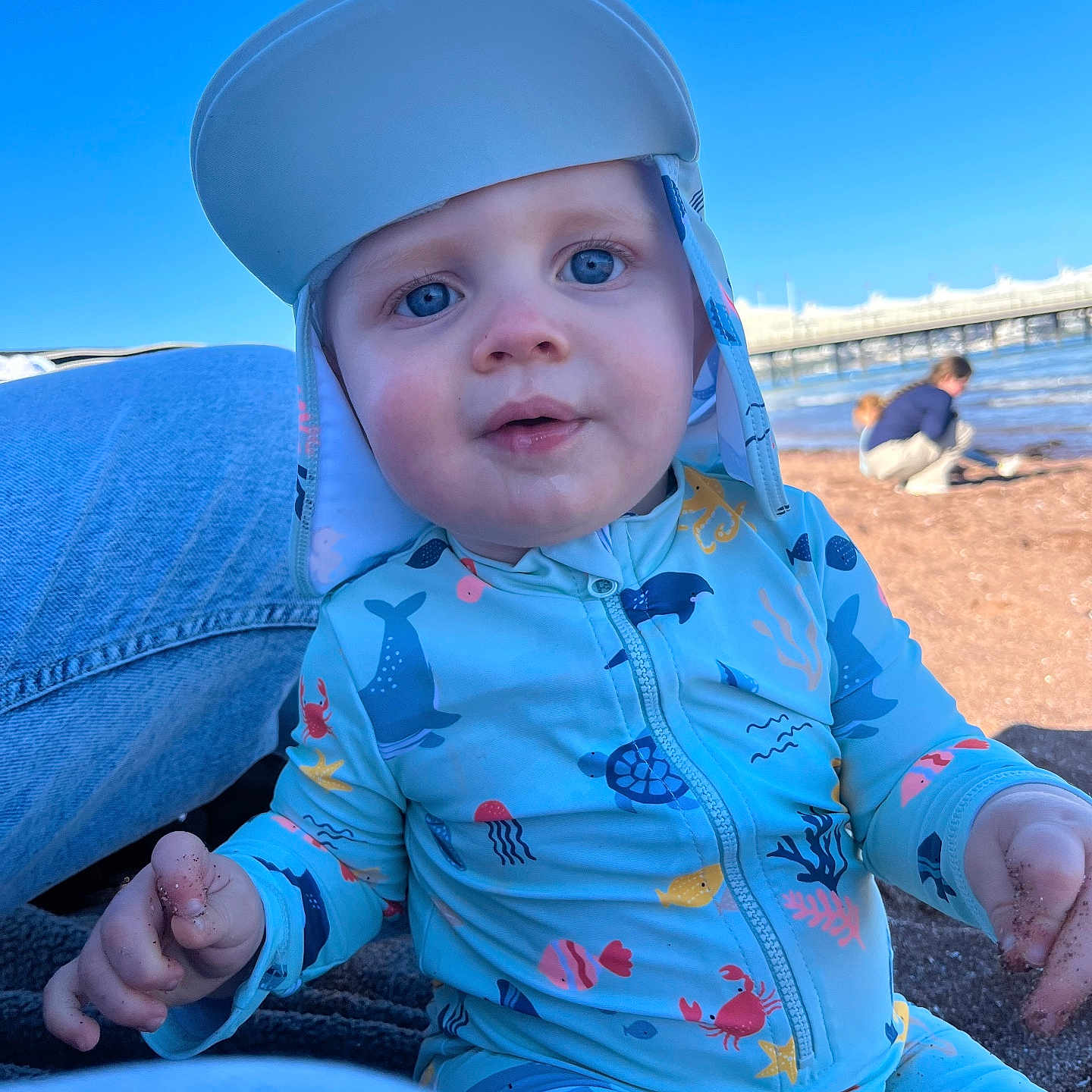 Oaklyn-Jay joined the competition — help win amazing prizes! baby, beach, blue_sky, child, closeup, curious, cute, daytime, hat, infant, marine_life_pattern, outdoor, person, pier, playing, sand, sitting, sunny, swimsuit, water
