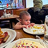 baby, bacon, breakfast, child, coat, curious, diner, food, glass_of_water, high_chair, indoor, ketchup, pancake, plate, sausage, scrambled_eggs, seat, sprinkles, table, window