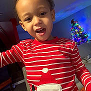 Chavae joined the competition — help win amazing prizes! child, toddler, smiling, red_shirt, striped_clothing, santa_claus_patch, christmas_tree, holiday_decor, indoor, living_room, basketball, curly_hair, young_child, person, festive, colorful_lights, happy, portrait, casual, home