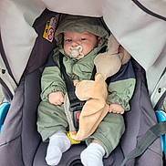 Liam a rejoint le concours — aidez-le/la à gagner de superbes lots ! baby, stroller, pacifier, plush_toy, green_jacket, white_socks, infant, child, seatbelt, car_seat, hood, cute, outdoor, person, small_hands, soft_toy, comfort, resting, casual_clothing, infant_care