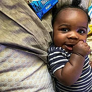 Komazia is registered to the contest to win money with this photo: baby, child, infant, striped_shirt, hand, smile, face, hair, mohawk, bed, pillow, blanket, snack, rice_krispies_treats, food, lying_down, cute, happy, indoors, portrait