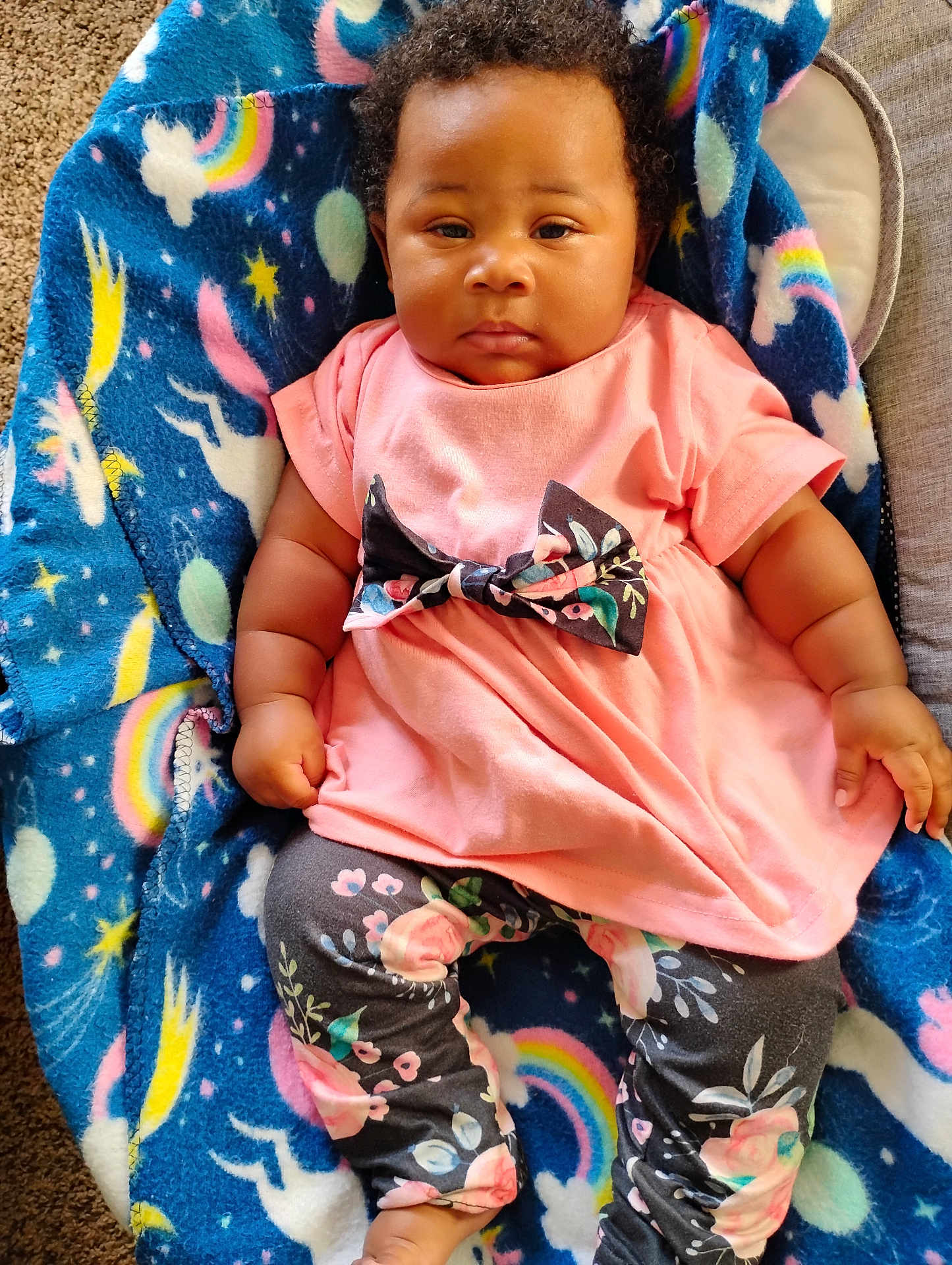 Amelia joined the competition — help win amazing prizes! baby, infant, child, blanket, blue_blanket, rainbow, unicorn, stars, pink_dress, bow, floral_pattern, leggings, carpet, curly_hair, sitting, indoors, cute, portrait, person, comfortable