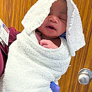 Treazure is registered to the contest to win money with this photo: newborn, baby, towel, wrapped, sleeping, hand, glove, person, indoor, door, wood, white, purple_glove, infant, cute, cozy, portrait, skin, face, holding