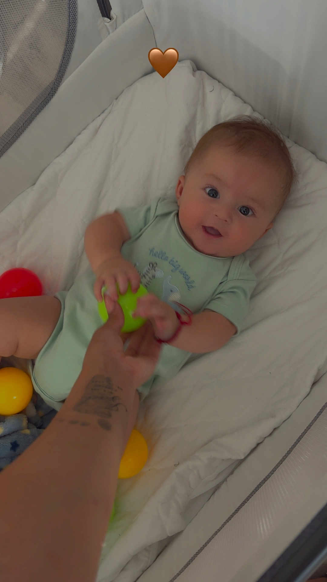 Izael joined the competition — help win amazing prizes! baby, crib, colorful_balls, hand, tattoo, green_ball, red_ball, yellow_ball, blanket, onesie, infant, smiling, child, indoor, playtime, cute, person, baby_toys, soft_bedding, happy