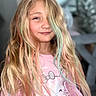 child, girl, portrait, smiling, long_hair, blonde_hair, colorful_hair, pastel_hair, pink_shirt, cat_shirt, indoors, close_up, face, eyes, hair, fashion, cute, casual, seated, home