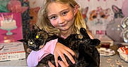 Mckenna joined the competition — help win amazing prizes! child, girl, cat, cats, pet, birthday, party, portrait, smiling, hugging, indoors, pink_shirt, blonde_hair, black_cat, tortoiseshell_cat, birthday_cake, decorations, balloons, table, cat_theme
