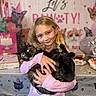 child, girl, cat, cats, pet, birthday, party, portrait, smiling, hugging, indoors, pink_shirt, blonde_hair, black_cat, tortoiseshell_cat, birthday_cake, decorations, balloons, table, cat_theme