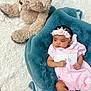 baby, infant, pink_outfit, headband, flower_crown, unicorn, plush_toy, teddy_bear, blue_blanket, white_rug, soft_texture, cute, child, portrait, lying_down, indoor, adorable, cozy, small_hands, small_feet