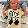 Everett is registered to the contest to win money with this photo: newborn, baby, infant, portrait, lying_down, face, smiling, clothing, onesie, mittens, sunglasses, text_on_clothing, bed, bedding, blanket, pacifier, indoor, close_up, playful, safe