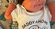 Everett is registered to the contest to win money with this photo: newborn, baby, infant, child, smiling, face, portrait, lying_down, indoors, blanket, clothing, onesie, hat, cap, red, black, white, text, patterned_background, close_up