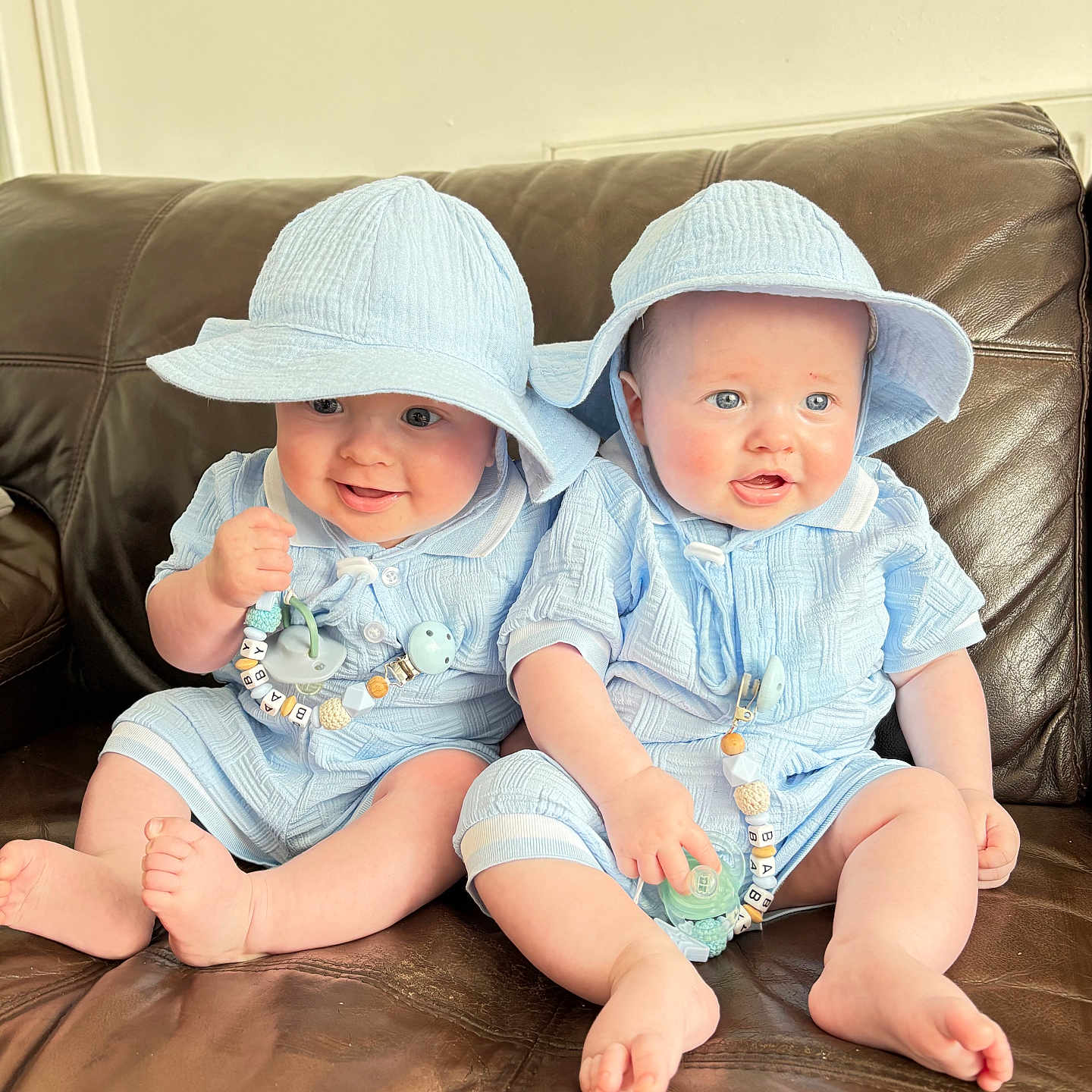 Luca And Jude joined the competition — help win amazing prizes! baby, blue_outfit, bright_eyes, child, chubby_cheeks, couch, cute, happy, hat, holding_object, indoors, infant, leather, matching_clothes, pacifier, person, portrait, sitting, smile, twin