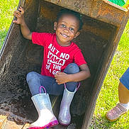 Taelyn is registered to the contest to win money with this photo: child, smiling, red_shirt, boots, excavator_bucket, rust, grass, outdoor, play, happy, sunlight, person, casual_clothing, fun, feet, toy, nature, daylight, kid, joy