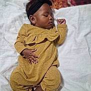 Amari is registered to the contest to win money with this photo: baby, infant, child, sleeping, blanket, headband, yellow_clothing, hands, feet, portrait, indoors, soft_texture, cozy, cute, peaceful, closeup, skin, person, relaxing, lying_down
