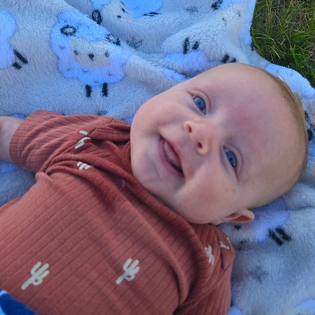 River joined the competition — help win amazing prizes! baby, smiling, blue_eyes, blanket, sheep_pattern, grass, outdoor, cute, infant, cactus_print, clothing, lying_down, happy, child, portrait, soft_texture, nature, toddler, face, young_child