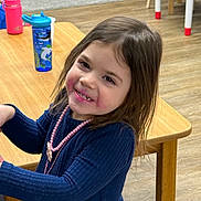 Layla joined the competition — help win amazing prizes! child, girl, smiling, face, long_hair, blue_dress, necklace, table, wooden_table, water_bottle, pink_bottle, floor, indoor, playroom, furniture, happy, person, cute, young, rosy_cheeks